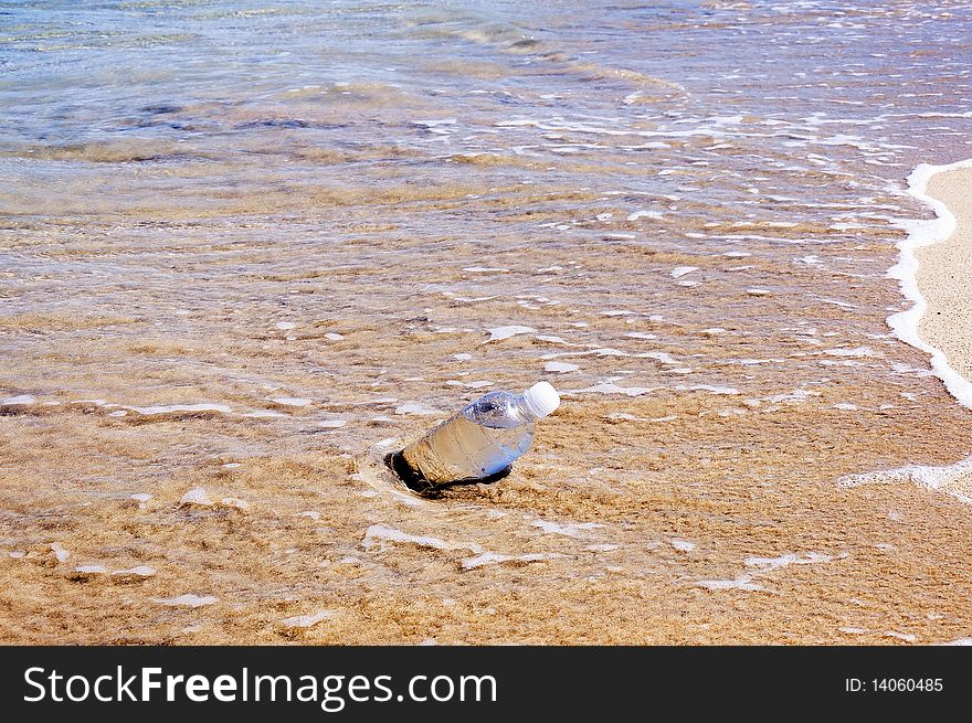 A bottle of water thrown on the shore of the ocean and is washed by waves