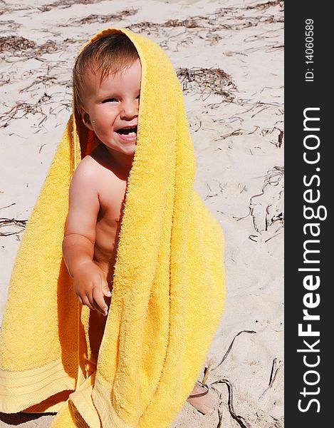 Charming little girl in a yellow towel on the beach as a symbol of childhood happiness and joy