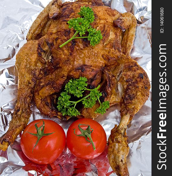 An image of a freshly roasted, spiced, organic chicken with tomatoes and parsley shown on silver foil. An image of a freshly roasted, spiced, organic chicken with tomatoes and parsley shown on silver foil.