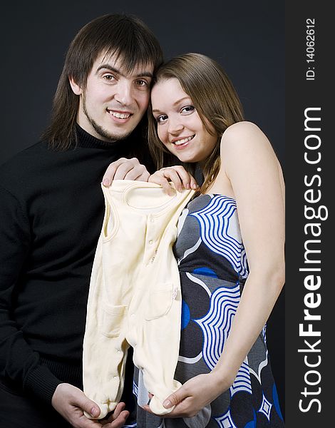 Pregnant couple embrace holding baby clothes. Pregnant couple embrace holding baby clothes