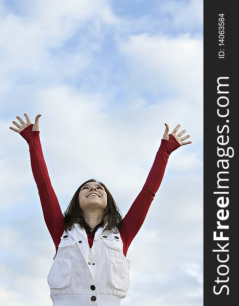 Female wearing red shirt and white vest, reaching both arms up to a blue cloudy sky. Female wearing red shirt and white vest, reaching both arms up to a blue cloudy sky