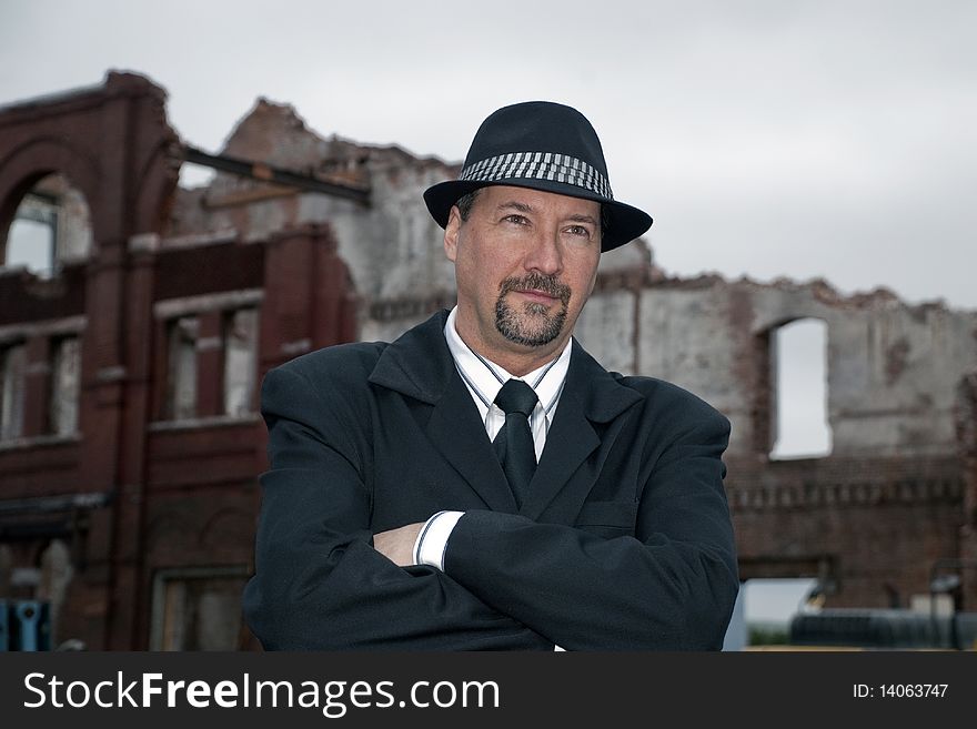Business man wearing a suit and hat, with his arms folder. a middle aged man with a beard and mustache standing in front of an old brick building ruins. light shy. Business man wearing a suit and hat, with his arms folder. a middle aged man with a beard and mustache standing in front of an old brick building ruins. light shy.