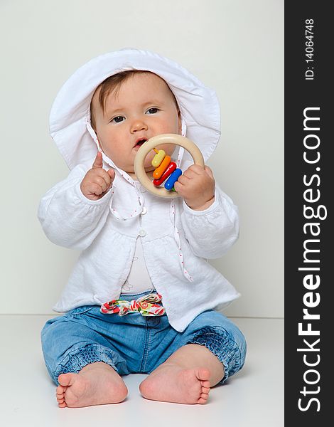 7 month old baby sitting with toy dressed in jeans and jumper