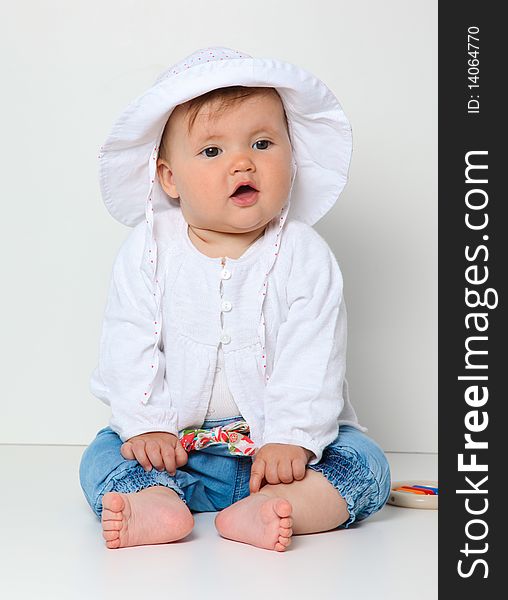 7 month old baby sitting with hat dressed in jeans and jumper