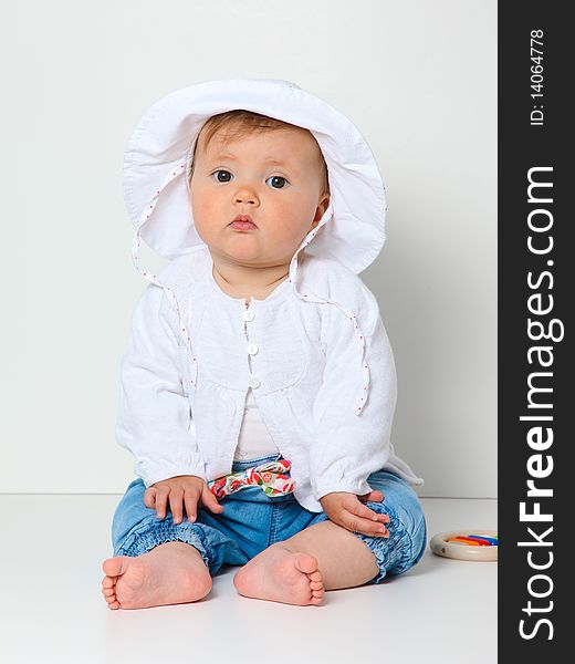 7 month old baby sitting with hat dressed in jeans and jumper