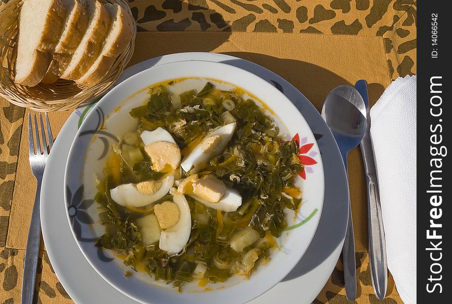 Plate with vegetable soup with eggs and bread on the orange tablecloth. Plate with vegetable soup with eggs and bread on the orange tablecloth