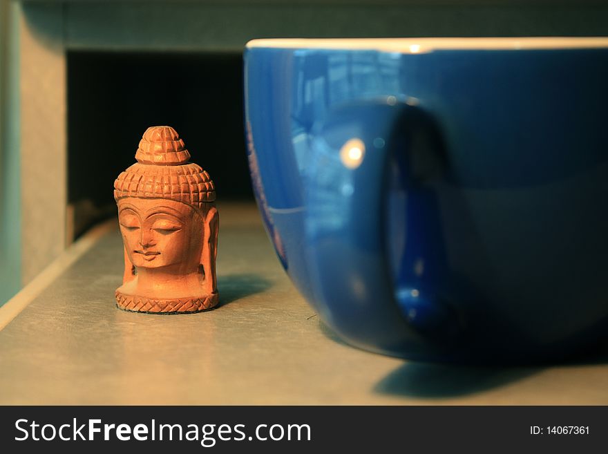 A Buddha head looks through a blue coffee mug. A Buddha head looks through a blue coffee mug