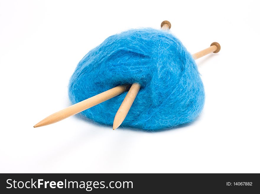 A large ball of blue mohair wool pierced with large wooden knitting needles against white.