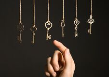 Woman Choosing Among Bronze Vintage Ornate Keys Hanging On Threads Against Dark Background Stock Images