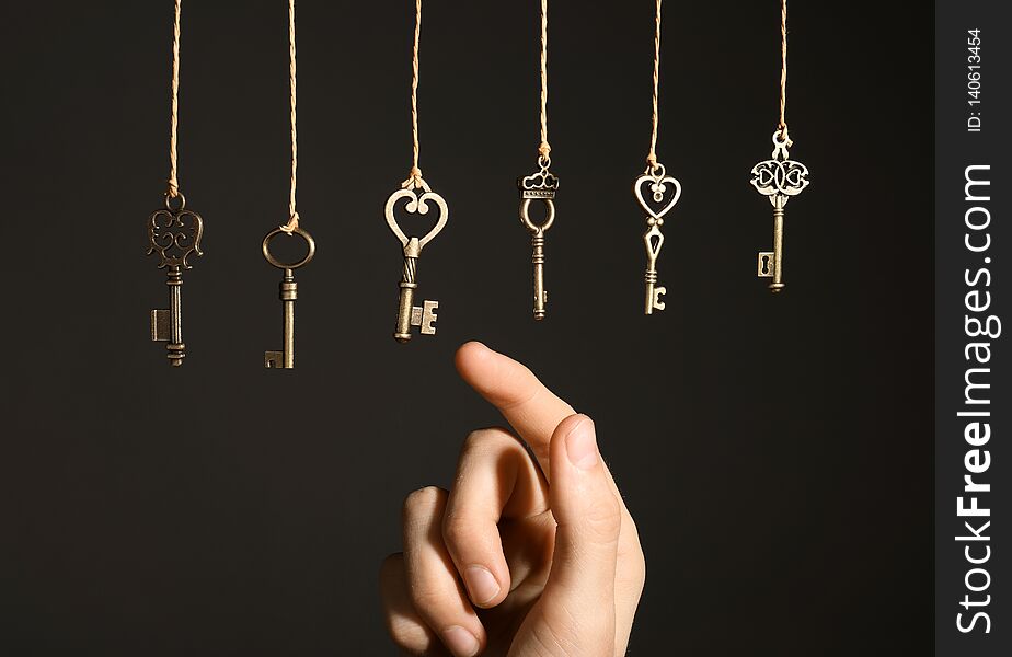 Woman Choosing Among Bronze Vintage Ornate Keys Hanging On Threads Against Dark Background