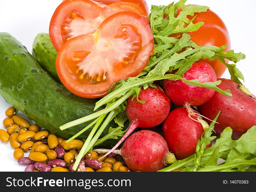 Fresh tomatoes, cucumbers, radishes, colorful beans and arugula on the white background, close-up, one tomato cut, all vegetables are coverd with drops of water. Fresh tomatoes, cucumbers, radishes, colorful beans and arugula on the white background, close-up, one tomato cut, all vegetables are coverd with drops of water.