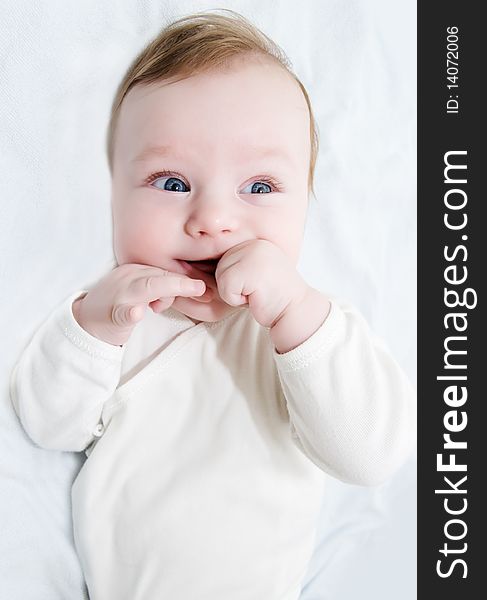 Adorable laughing baby boy lying with hands in his mouth