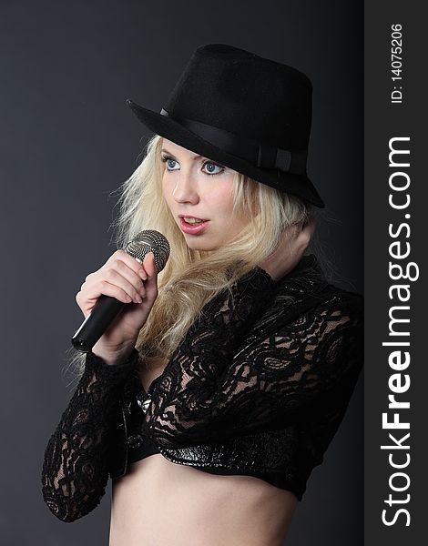 Singing blond girl in black hat with microphone