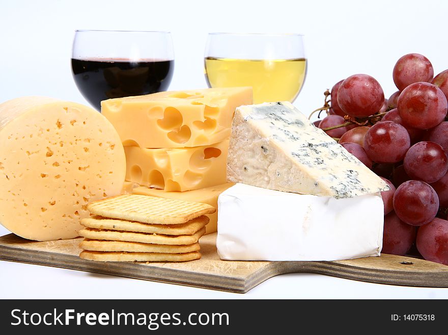 Various types of cheese (swiss, yellow, brie, blue cheese) with red and white wine, red grapes and crackers in close up on white background