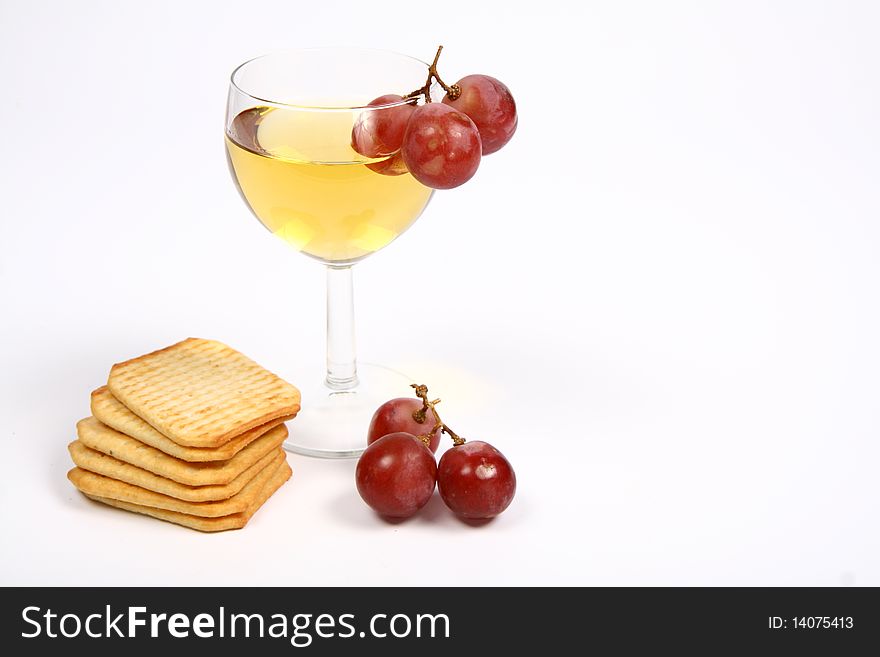 White wine in a wineglass with red grapes and some crackers on white background with space for text. White wine in a wineglass with red grapes and some crackers on white background with space for text