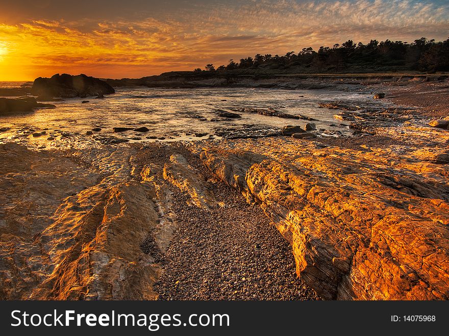 A rocky beach is cast in a gold glow from the setting sun by the Pacific Ocean. A rocky beach is cast in a gold glow from the setting sun by the Pacific Ocean