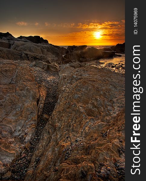 A vertical shot showing the rocky details along the beach with the sun setting over the Pacific Ocean. A vertical shot showing the rocky details along the beach with the sun setting over the Pacific Ocean