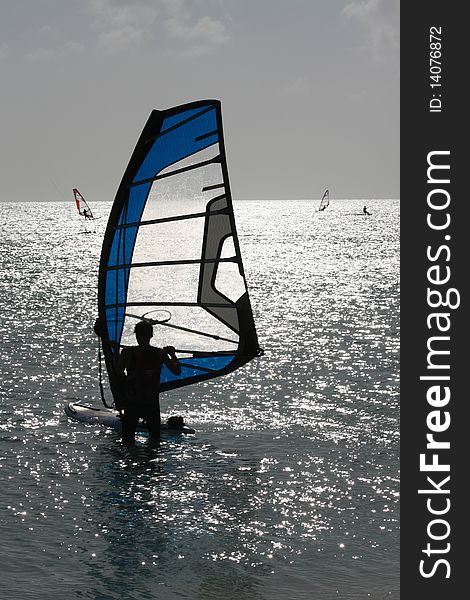 Silhouette of a windsurfer setting up to go. Other surfers present in background. Silhouette of a windsurfer setting up to go. Other surfers present in background.