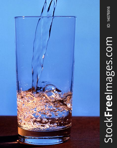 Water is being poured into glass against a blue background. Vertical shot. Water is being poured into glass against a blue background. Vertical shot.