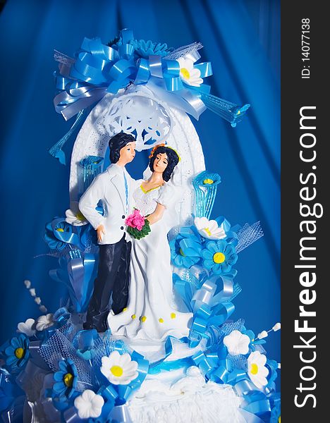 Couple on wedding cake against blue curtain