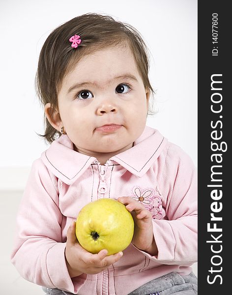 Sulky baby girl holding a green apple in her hands thinking and looking up.Check also Children. Sulky baby girl holding a green apple in her hands thinking and looking up.Check also Children