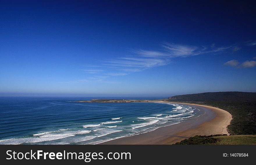 Landscape view of a deserted beach with rows of white breakers and a brilliant clear blue sky with an odd white cloud wisp. Landscape view of a deserted beach with rows of white breakers and a brilliant clear blue sky with an odd white cloud wisp