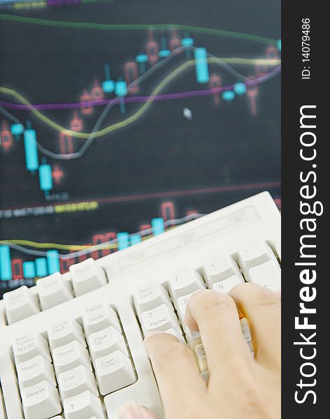 A hand operating keyboard , the background is the stock market graph