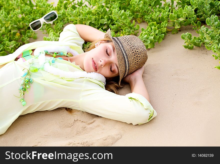 Attractive woman lying down on the sand wearing a hat and white sunglasses. Attractive woman lying down on the sand wearing a hat and white sunglasses.