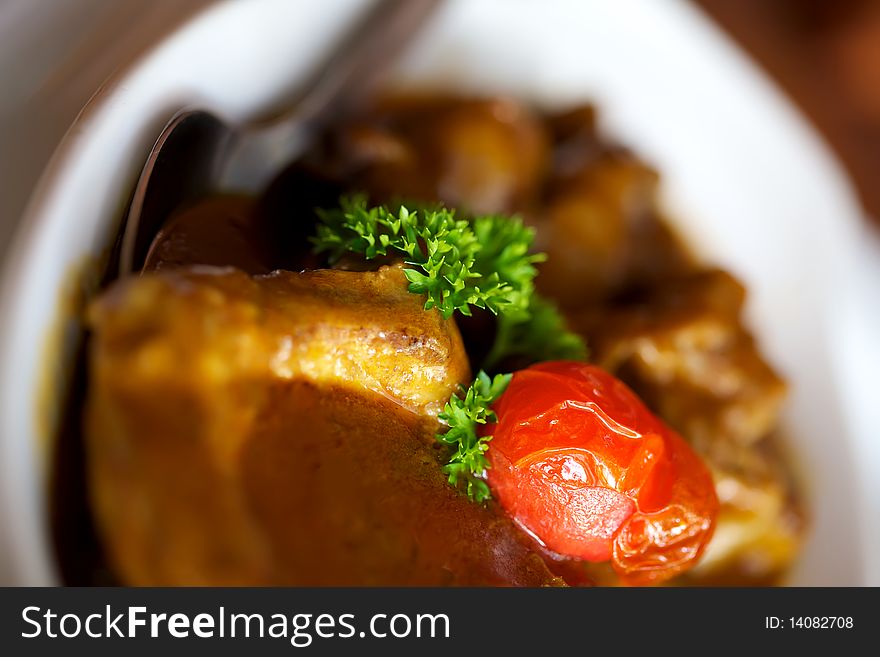 Closeup shot of a saucy lamb tjop in a bowl with a red tomato ontop. Closeup shot of a saucy lamb tjop in a bowl with a red tomato ontop