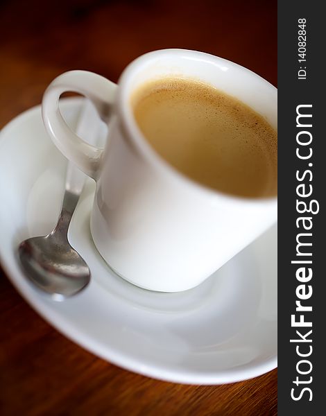 Espresso in a saucer with a spoon taken on a coffee shop table.