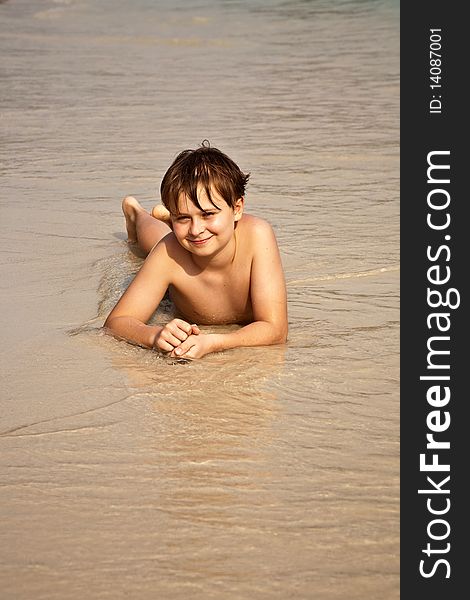 Boy iy lying at the beach and enjoying the warmness of the water and looking self confident and happy. Boy iy lying at the beach and enjoying the warmness of the water and looking self confident and happy