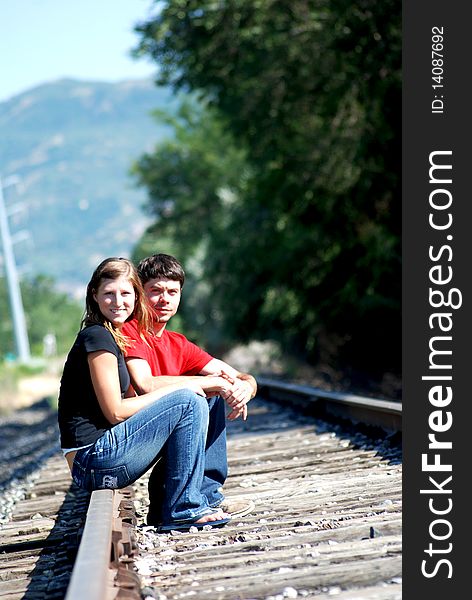 This is a photo of a couple holdings hands while sitting down on railroad tracks. This is a photo of a couple holdings hands while sitting down on railroad tracks.