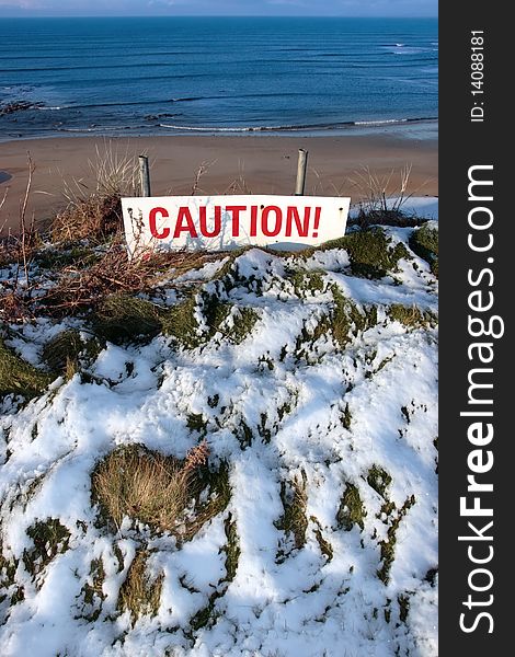 A red caution sign on a cliff edge in snow covered ballybunion. A red caution sign on a cliff edge in snow covered ballybunion