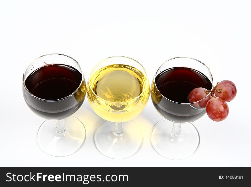 Red and white wine in wineglasses with three red grapes on white background with space for text