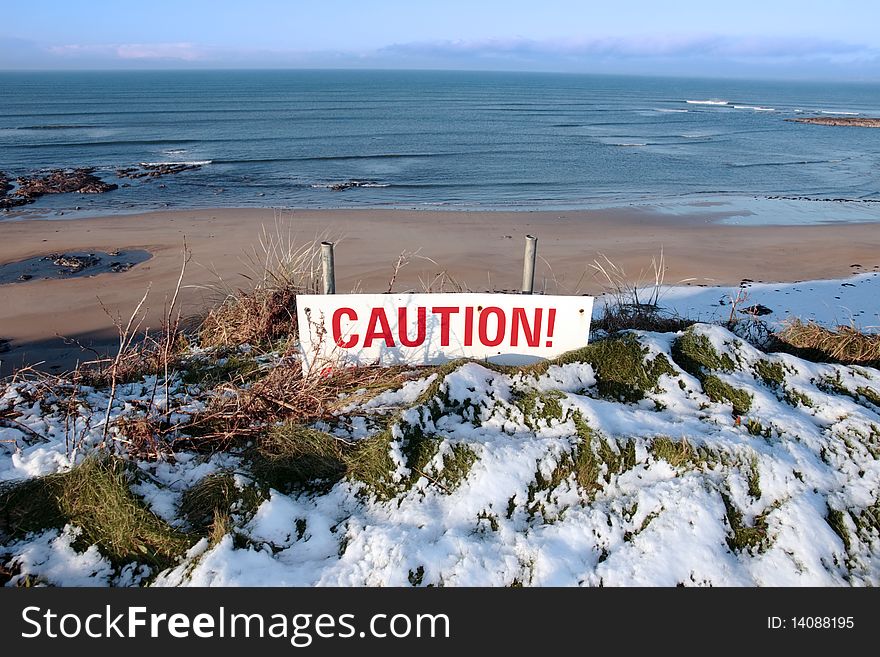 A red caution sign on a cliff edge in snow covered ballybunion. A red caution sign on a cliff edge in snow covered ballybunion