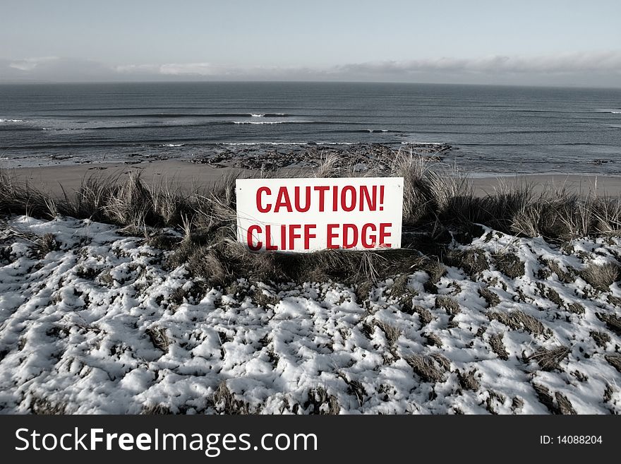 A red caution sign on a cliff edge in snow covered ballybunion. A red caution sign on a cliff edge in snow covered ballybunion