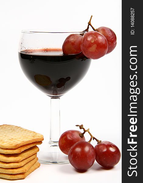 Red wine in a wineglass with red grapes and some crackers on white background