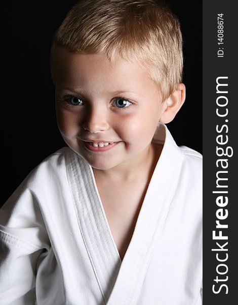 Young boy wearing his karate uniform on a black background. Young boy wearing his karate uniform on a black background