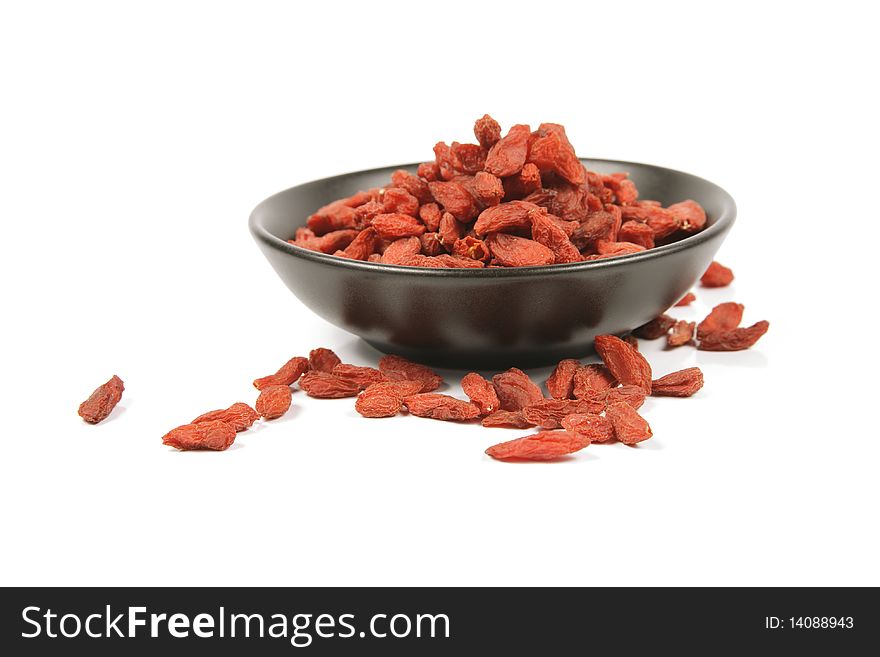 Red dry goji berries in a small black dish on a reflective white background. Red dry goji berries in a small black dish on a reflective white background