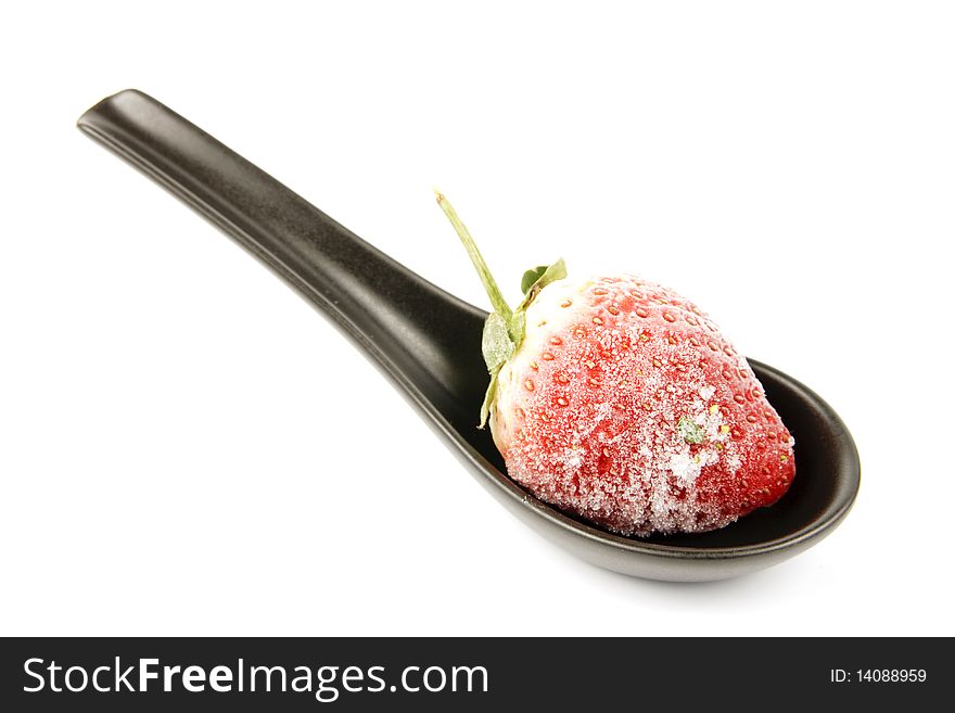 Red ripe frozen strawberry on a small black spoon with a reflective white background. Red ripe frozen strawberry on a small black spoon with a reflective white background