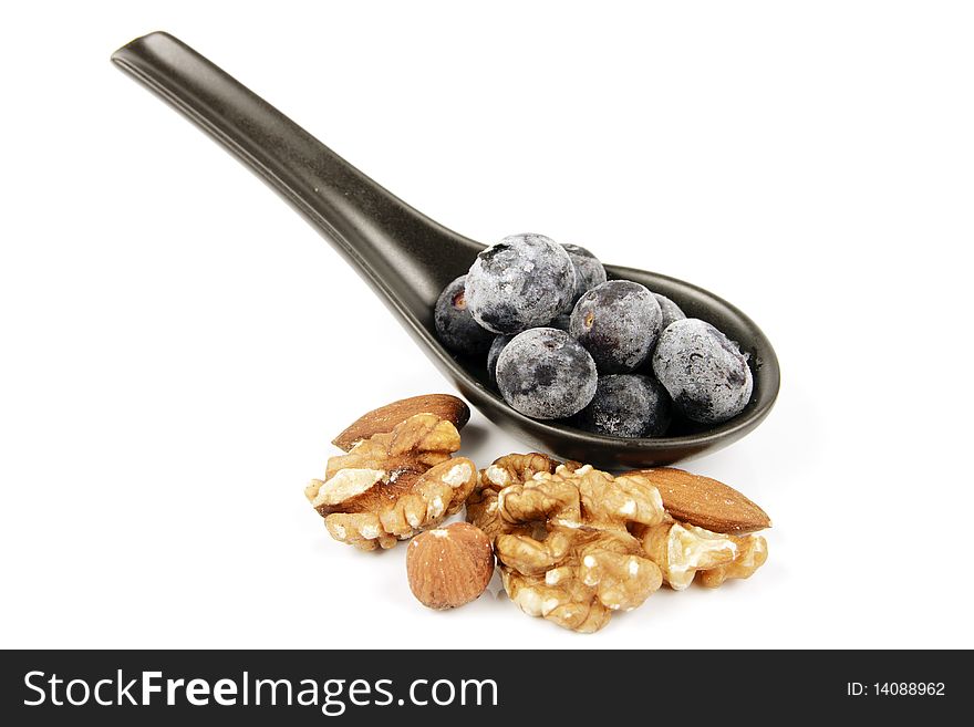 Blue ripe blueberries on a small black spoon with mixed nuts on a reflective white background. Blue ripe blueberries on a small black spoon with mixed nuts on a reflective white background