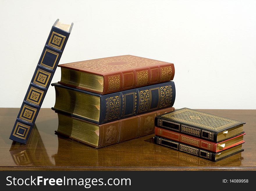 A pile of classic leather bound books with gold designs on the cover.