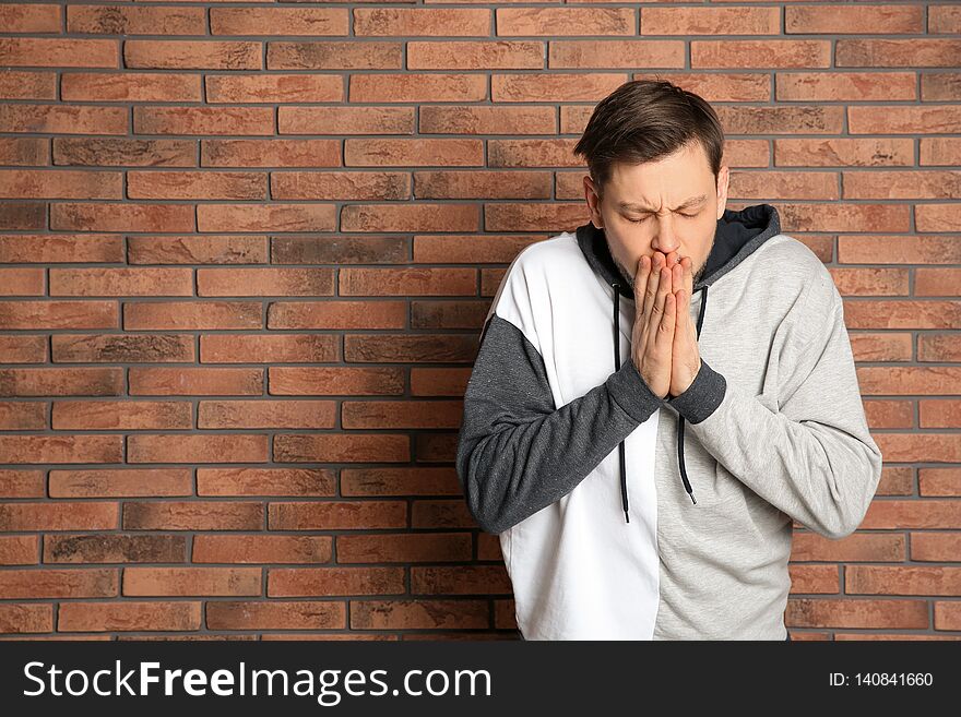 Man suffering from cold near brick wall.