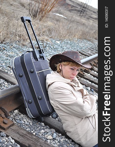 Young blond woman in a bright jacket sits on rails and is 
based on a large travel bag on wheels, cowboy style, bag with wheels tilted, a pen nominated. Young blond woman in a bright jacket sits on rails and is 
based on a large travel bag on wheels, cowboy style, bag with wheels tilted, a pen nominated