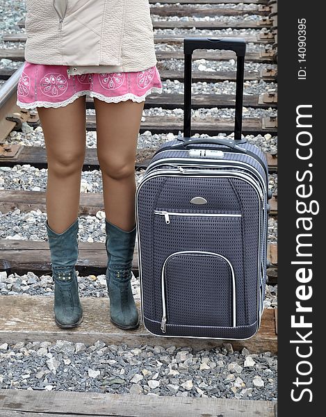 Slender legs of a woman passenger and the bag, standing on railroad tracks. Slender legs of a woman passenger and the bag, standing on railroad tracks