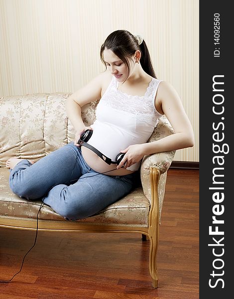 The image of a pregnant woman lying on the sofa and listening to music with headphones. The image of a pregnant woman lying on the sofa and listening to music with headphones