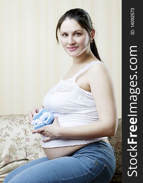The image of a pregnant woman on the couch with blue booties in the hands of