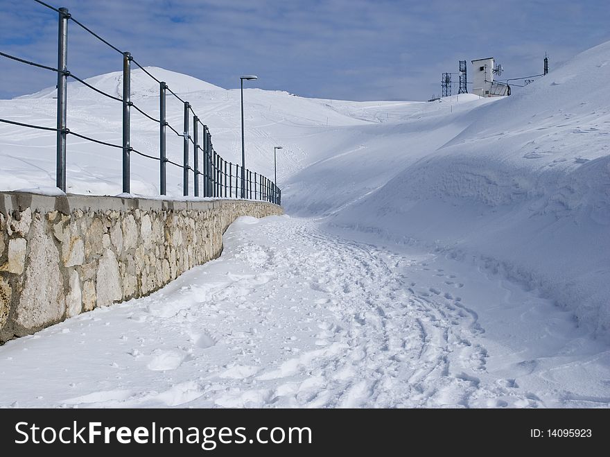 Snow path in mountains with a small brick wall. Snow path in mountains with a small brick wall