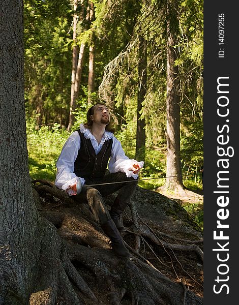 Man in historical costume sits on the roots of a tree