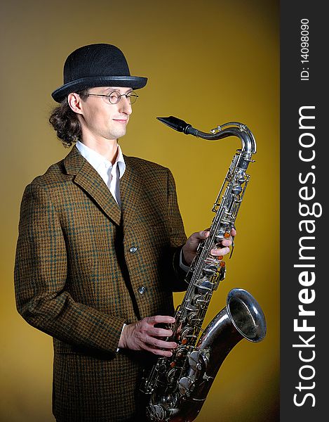 Portrait of young english gentleman in bowler hat holding saxophone. yellow background. Portrait of young english gentleman in bowler hat holding saxophone. yellow background